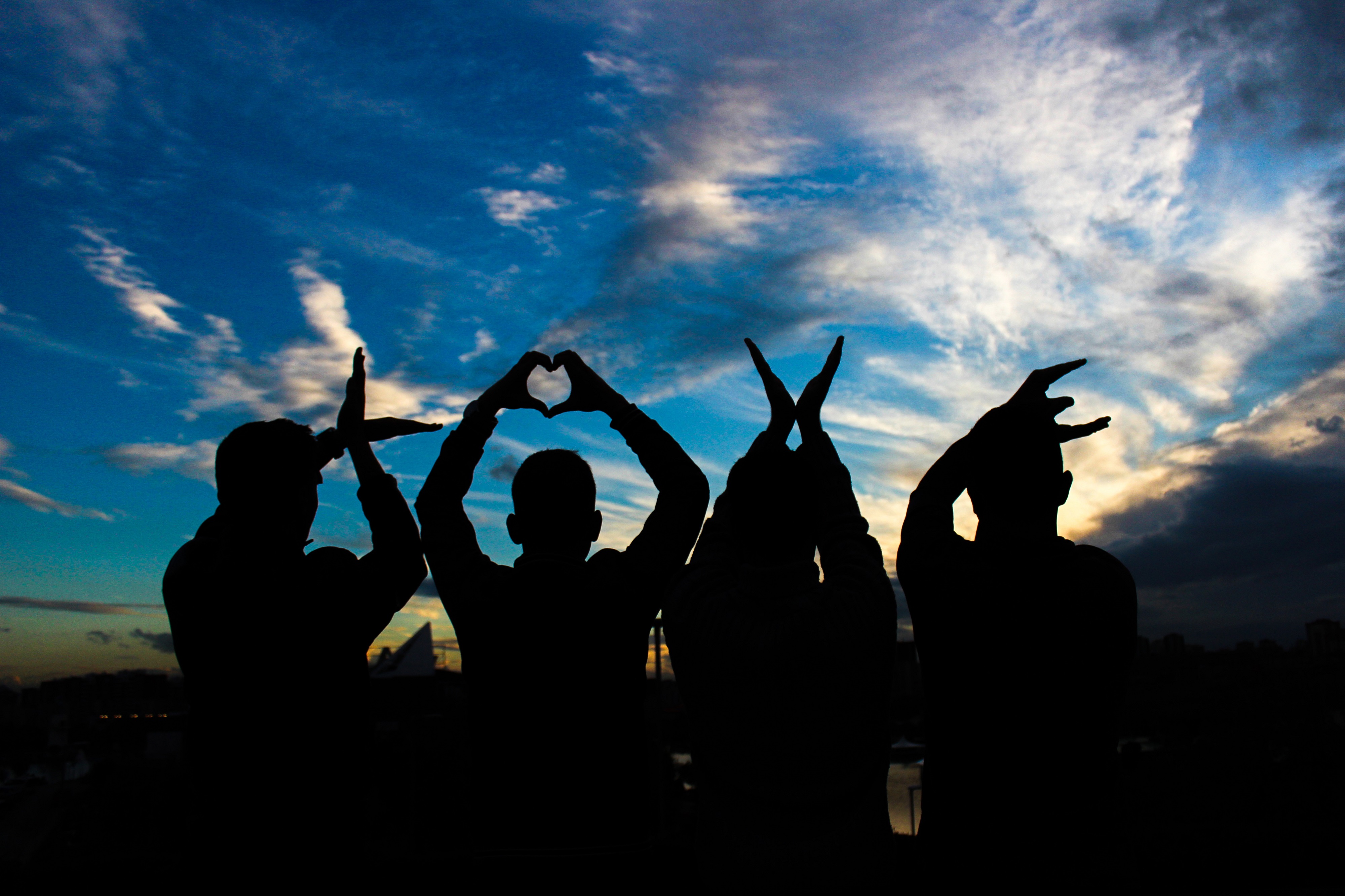 Silhouette of four people holding hands above their heads to spell out the word "love"